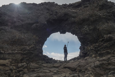 Low angle view of man standing on rock formation while taking selfie