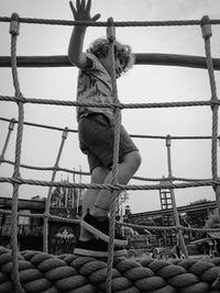 Low angle view of boy walking on rope against sky