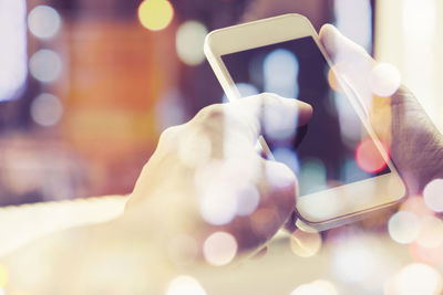 Close-up of hand holding smart phone seen through glass with reflection