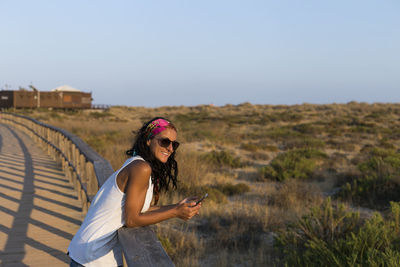 Portrait of smiling woman holding phone on footbridge