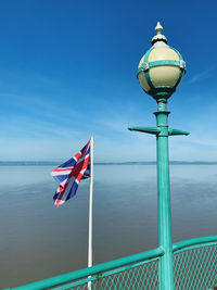 Flag on street light by sea against blue sky