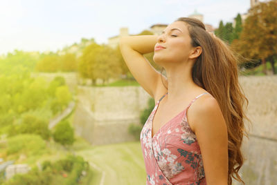 Side view of young woman with hand in hair standing outdoors