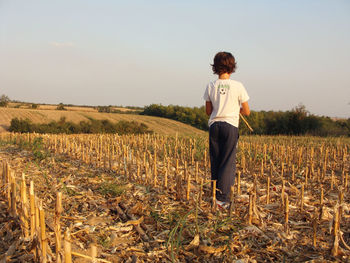 Rear view of child on farmed field against clear sky