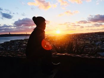 Side view of man standing by cityscape against sky during sunset