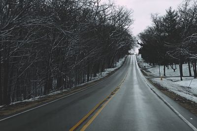 Empty road amidst bare trees against sky