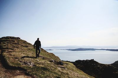 Mature man walking on mountain by sea against clear sky during sunny day