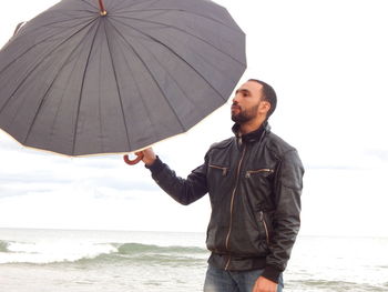 Man standing with black umbrella at beach