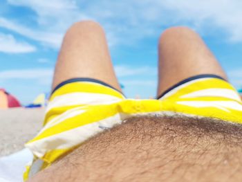 Midsection of man relaxing at beach against sky