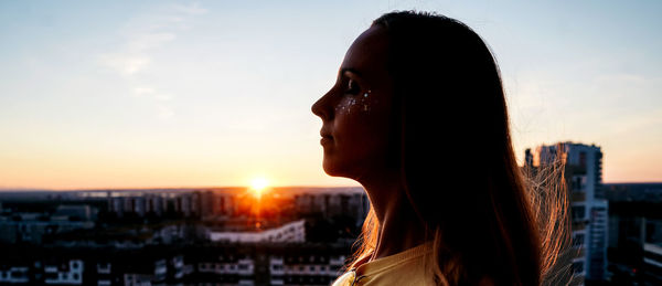 Side view of woman looking away against sky during sunset