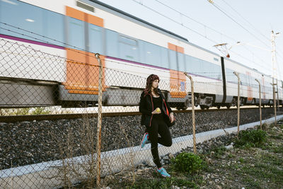 Woman leaning on chainlink fence against train