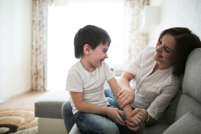 Beautiful brunette mom and son hugging on sofa in real interior, soft focus