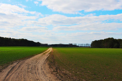 Dirt road amidst field against sky