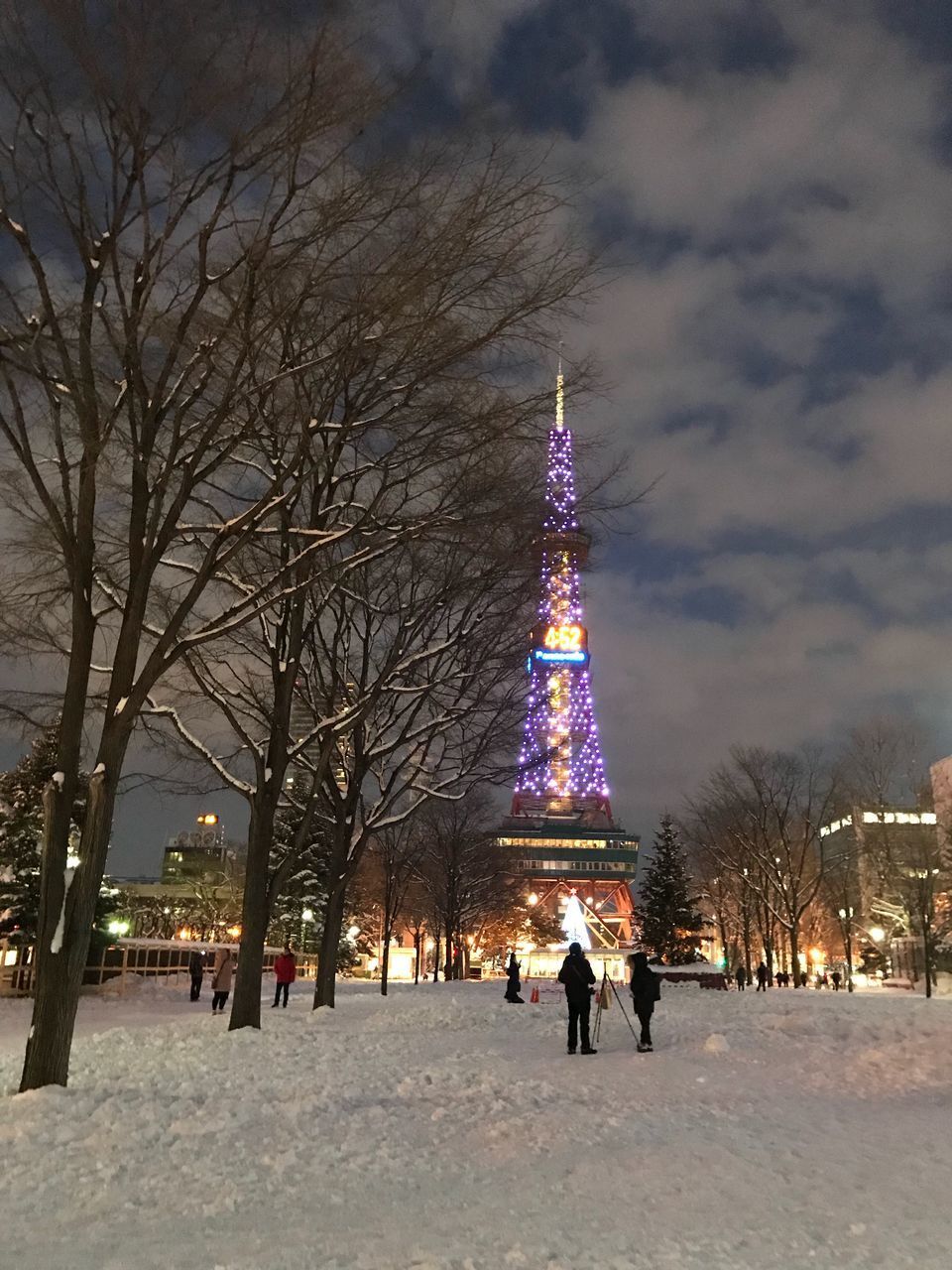 ILLUMINATED CHRISTMAS TREE IN SNOW COVERED CITY AGAINST SKY