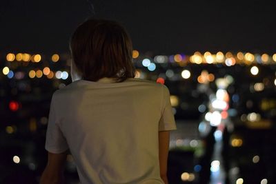 Rear view of boy in illuminated city at night