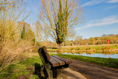 Empty bench in park by lake against sky