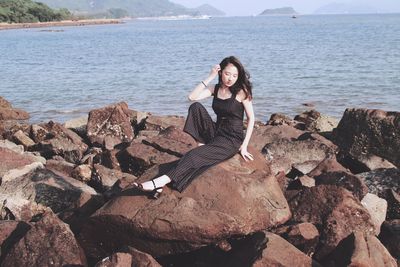Young woman sitting on rock by sea