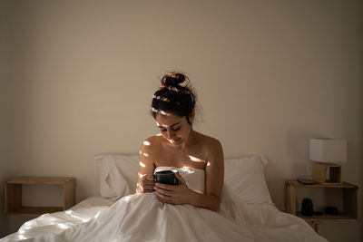 Young woman using mobile phone while sitting on bed