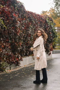 A beautiful happy girl in casual clothes is walking in the autumn outdoor park drinking coffee