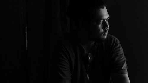 Young man looking away against black background