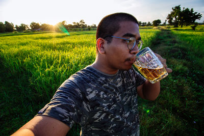 Midsection of young man drinking sunglasses on field