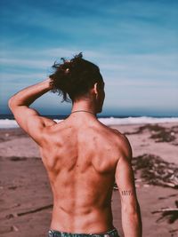 Rear view of shirtless man standing at beach against sky