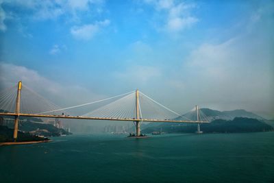 Suspension bridge over sea against cloudy sky