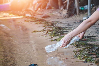 Cropped hands of woman holding bottles over dirt road