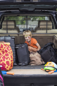 Boy sitting with luggage in car trunk