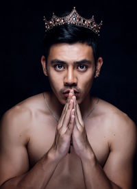 Close-up portrait of young man wearing crown against black background