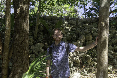 Portrait of man standing by tree trunk in forest