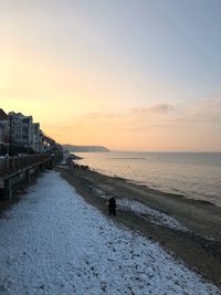 Snow covered beach against sky during sunset