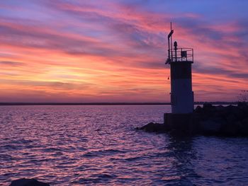 Lighthouse by sea against sky during sunset