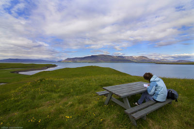 Woman reading book while sitting on picnic table by lake