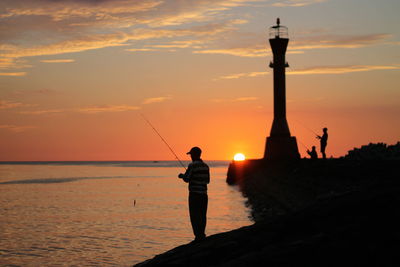 Silhouette man fishing by sea against sky during sunset