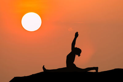 Silhouette woman exercising on field against orange sky during sunset