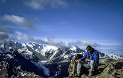 Man sitting on mountain against sky