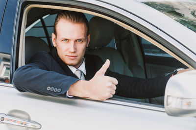 Portrait of businessman gesturing thumbs up while driving car