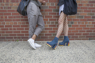 Legs of young women talking beside a brick wall