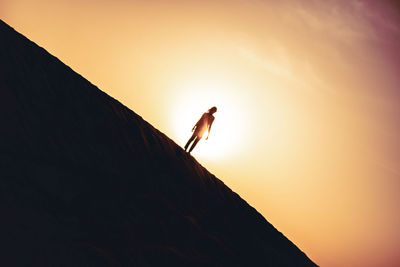 Low angle view of silhouette person standing on mountain against orange sky