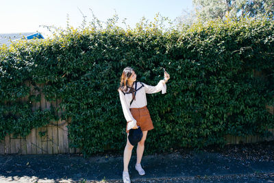 Woman taking selfie while standing against plants