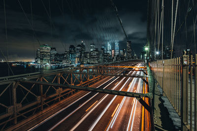 Light trails on bridge in city against sky at night
