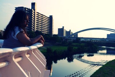 Man sitting on bridge over city against sky