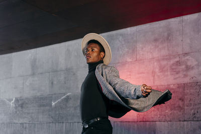 Young man looking away while standing against wall