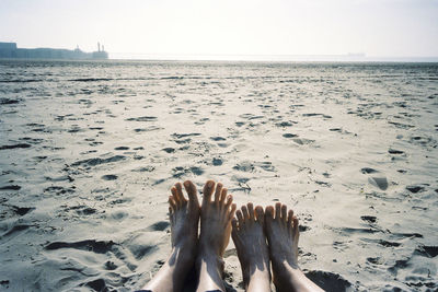 Low section of people relaxing on beach against sky