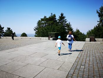 Rear view of boy with mother walking on footpath