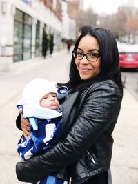 Portrait of mother carrying cute son while standing on sidewalk in city