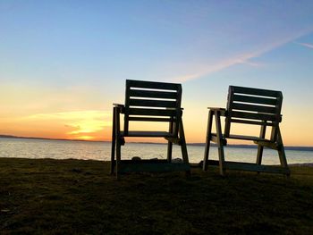 Chair on beach against sky during sunset