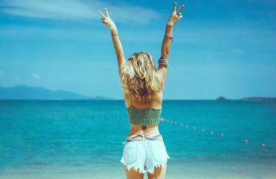 Rear view of woman standing at beach against sky