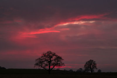 Silhouette trees on field against romantic sky at sunset