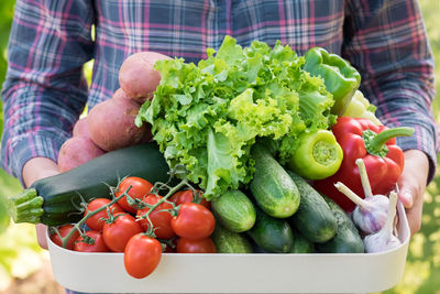 A female farmer holds a tray full of fresh raw vegetables. 